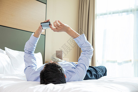 商务男性躺在酒店床上看手机图片