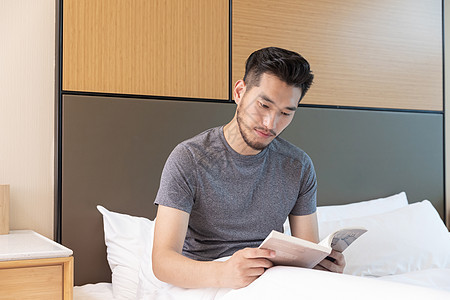 男性出差躺在酒店床上看书图片
