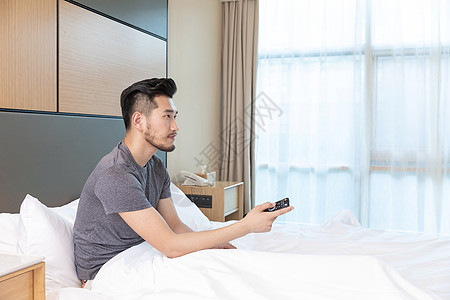 男性躺在酒店床上看电视图片