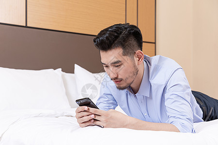 职业男性酒店出差趴床上玩手机图片素材