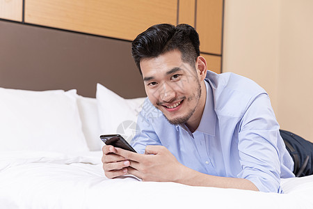 职业男性酒店出差趴床上玩手机图片
