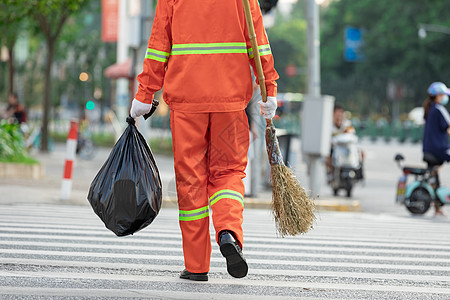 拎着垃圾袋与扫帚的环卫工人过马路背景图片