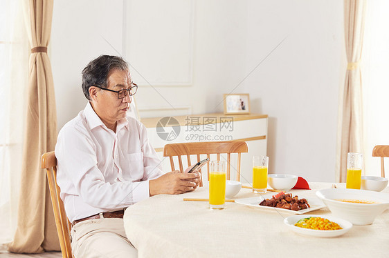 老年男性餐桌旁玩手机图片