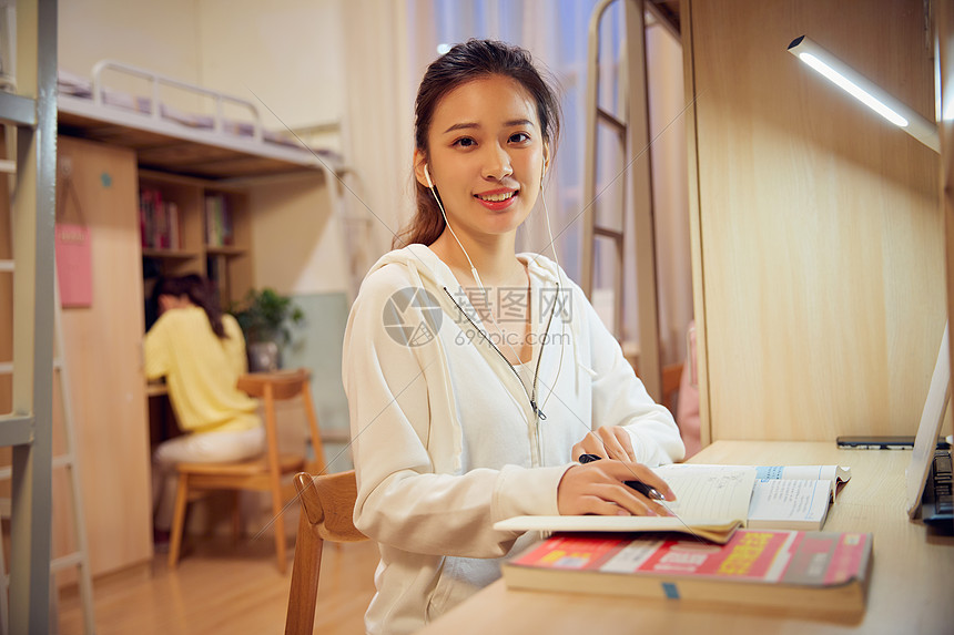 夜晚女学生戴着耳机在宿舍认真复习功课图片