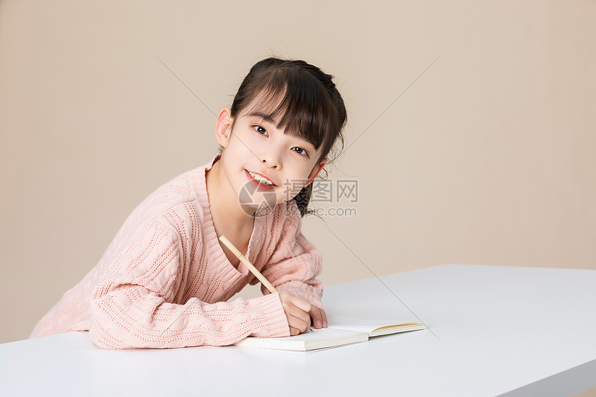 小女孩趴在桌子上写字做作业图片