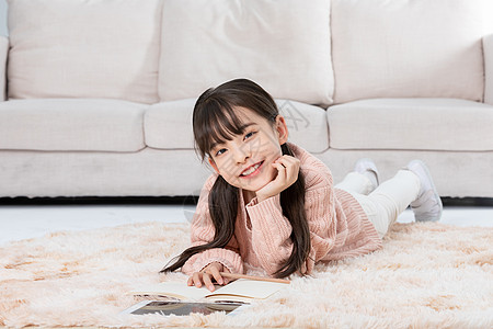 微笑的小女孩女孩趴在地毯上使用平板电脑背景