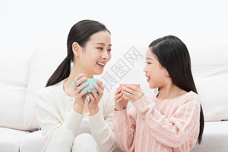 茶杯里小女孩母亲和女儿坐在沙发前喝水背景