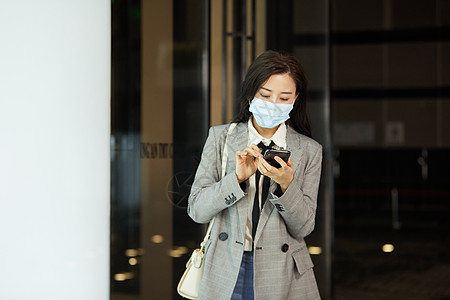 戴口罩的女白领下班低头玩手机背景图片