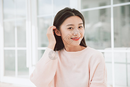 迷人清纯美女穿着粉色毛衣的美女对着镜头微笑撩头发背景