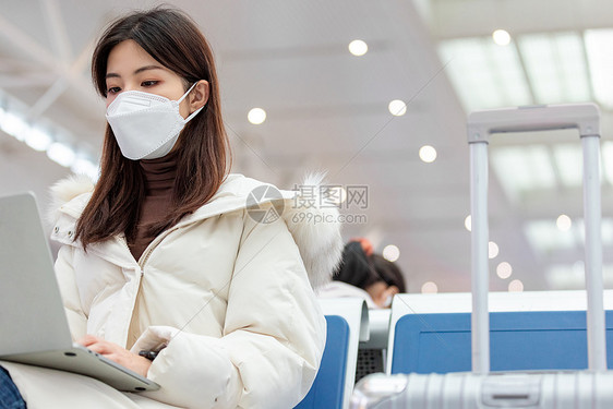 戴着口罩的女性在坐在等候厅使用笔记本电脑办公图片