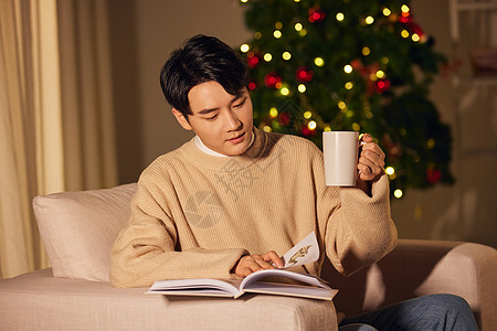 圣诞树夜晚年轻男士冬季在家阅读喝茶背景