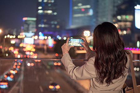 白领女性使用手机拍夜景的都市女性背景