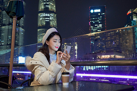 夜晚坐在咖啡厅玩手机的都市女孩图片