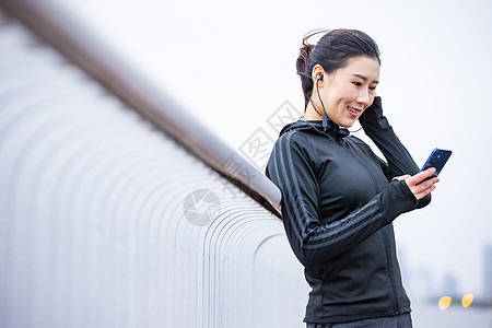 穿着健身衣的女性靠在栏杆上使用手机图片