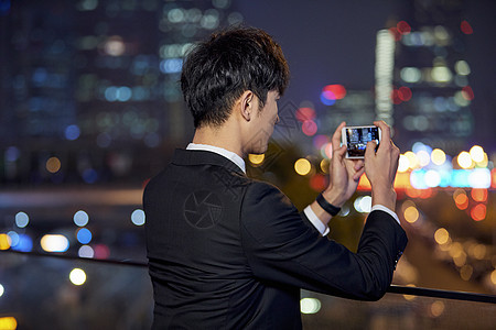 夜晚男青年用手机拍摄城市夜景背影图片