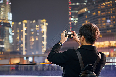 男青年用手机拍摄城市夜景图片