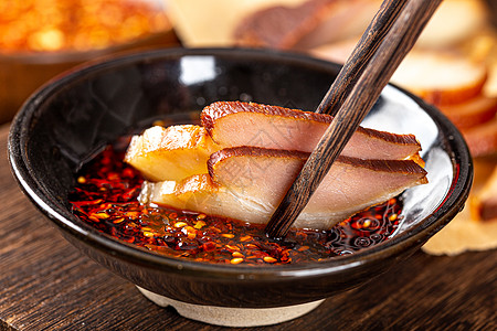 五花肉切片筷子将腊肉放入辣椒油中背景