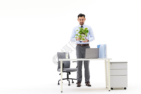 男性捧着一盆绿植站在办公桌前图片