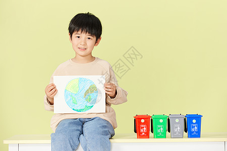 小男孩坐在分类垃圾桶模型旁边微笑图片