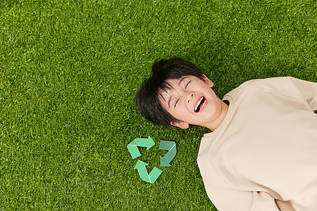 躺在草坪上的小男孩旁边放着可回收符号背景图片