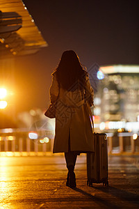 闹市区夜晚都市女性手提行李箱走在路上背景