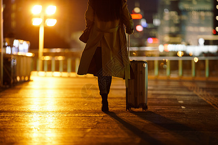 闹市区夜晚都市女性手提行李箱走在路上背景