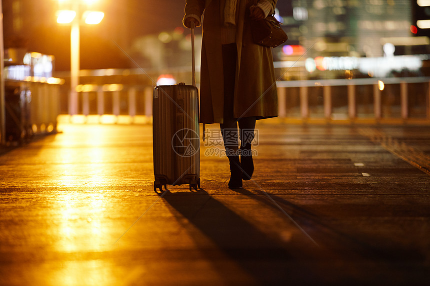 夜晚都市女性手提行李箱走在路上图片