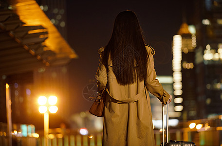 夜晚都市女性手提行李箱走在路上高清图片