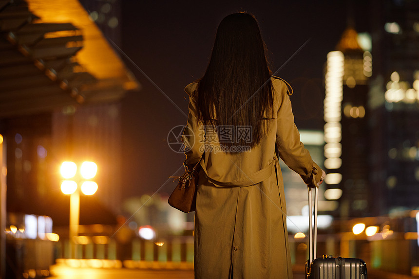 夜晚都市女性手提行李箱走在路上图片