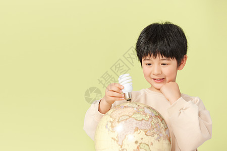 小男孩拿着节能灯泡放在地球模型上图片