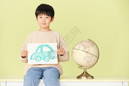 坐在桌上的小男孩拿着手绘的汽车图片图片