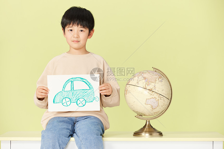 坐在桌上的小男孩拿着手绘的汽车图片图片