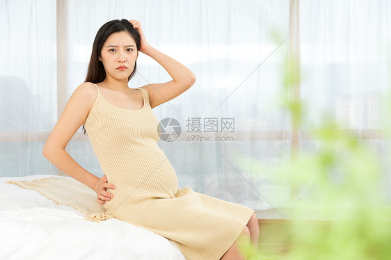 坐在床上表情烦恼的孕妇图片