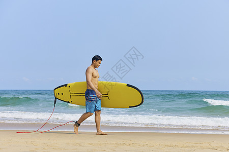 男青年手拿冲浪板海边行走高清图片