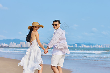 夏季旅游情侣年轻情侣牵手海边散步背景