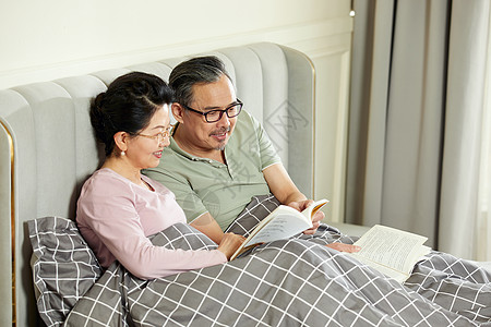 居家学习中老年夫妇坐在床上享受阅读的乐趣背景