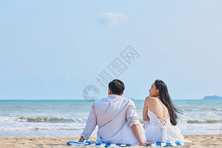 海边美女年轻情侣坐在沙滩看海背影背景