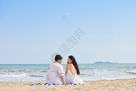 情侣牵手背影年轻情侣坐在沙滩对视背影背景