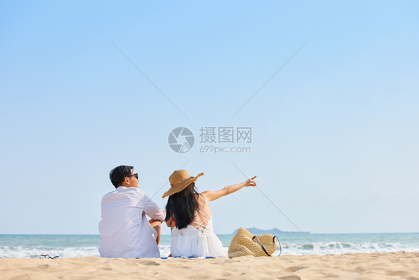 年轻情侣坐在沙滩看海背影