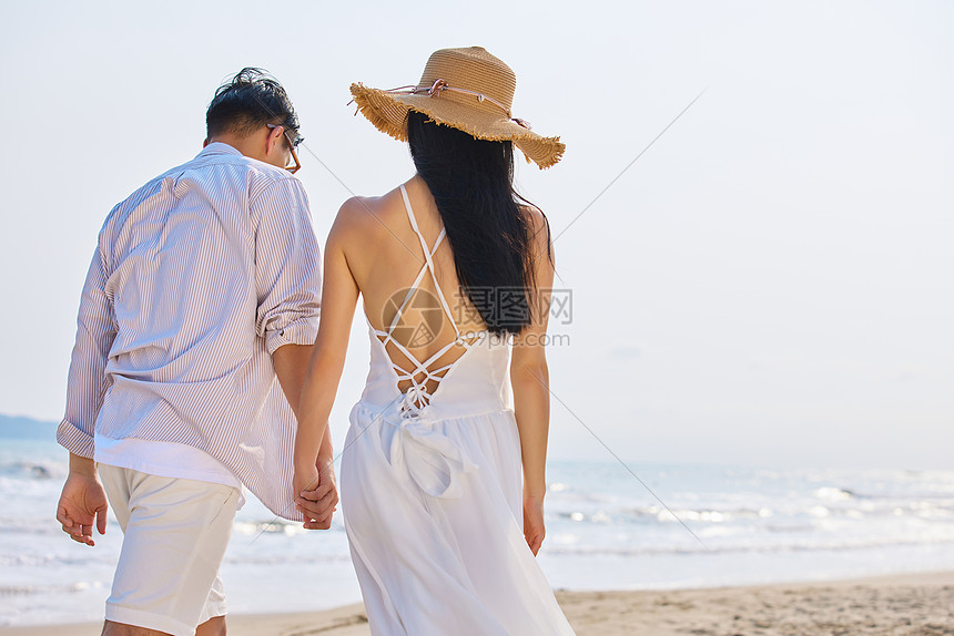 年轻情侣牵手海边散步背影