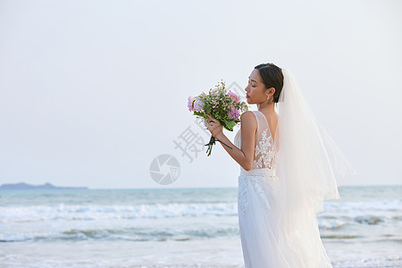 海边穿婚纱的美女手拿手捧花背影图片