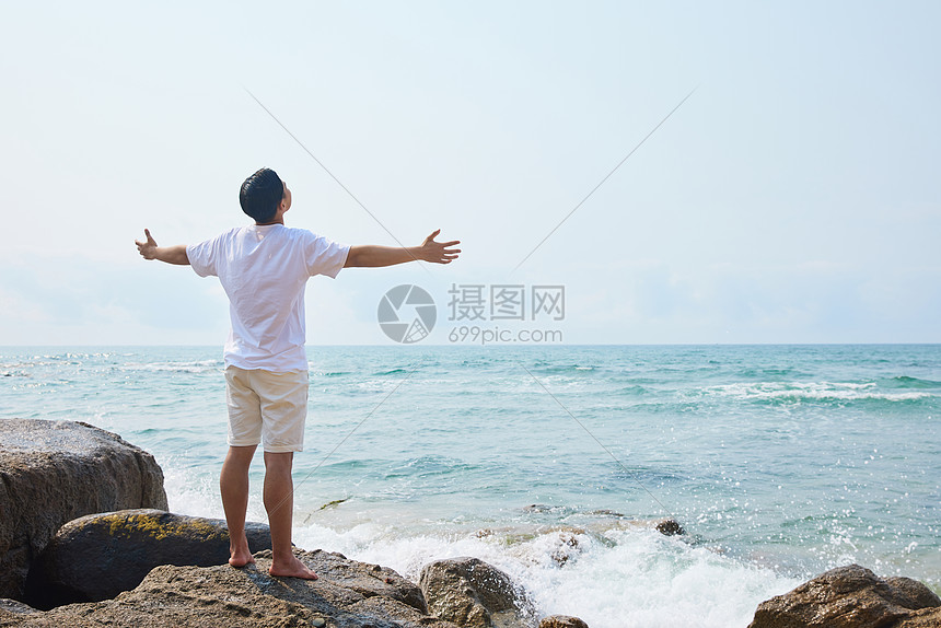男青年张开手臂拥抱大海背影