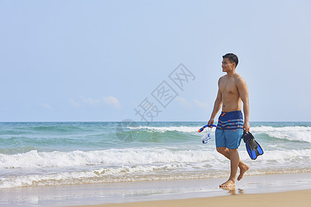 男青年拿着潜水装备在海边行走图片