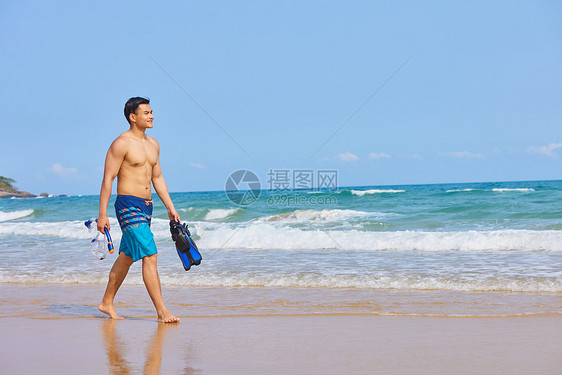 男青年拿着潜水装备在海边行走图片