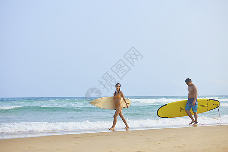 沙滩男女青年男女拿着冲浪板海边行走背景