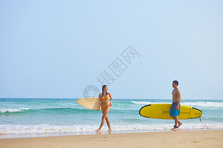 沙滩男女青年男女拿着冲浪板海边行走背景