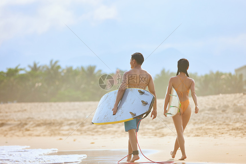 年轻男女拿着冲浪板海边行走背影图片
