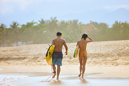 沙滩情侣年轻男女拿着冲浪板海边行走背影背景