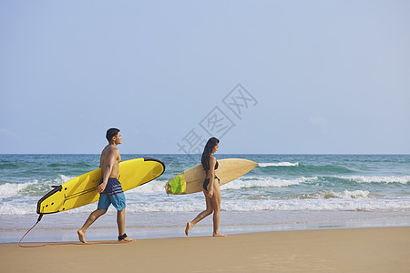 美女海边行走年轻男女拿着冲浪板海边行走背影背景