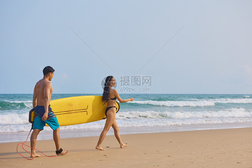 年轻男女拿着冲浪板海边行走背影图片